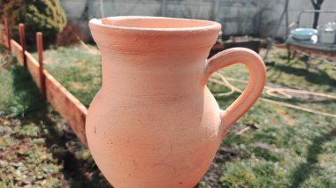 Antika kil sürahi. Ahşap bir çitin üzerindeki kil sürahi bahçedeki bir ağacın arka planına karşı. Kadim büyük kavanoz, içme suyu, su kaynağı, akan su, musluk suyu. Retro biçimi.