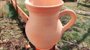 Antika kil sürahi. Ahşap bir çitin üzerindeki kil sürahi bahçedeki bir ağacın arka planına karşı. Kadim büyük kavanoz, içme suyu, su kaynağı, akan su, musluk suyu. Retro biçimi.