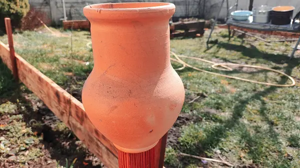 Antika kil sürahi. Ahşap bir çitin üzerindeki kil sürahi bahçedeki bir ağacın arka planına karşı. Kadim büyük kavanoz, içme suyu, su kaynağı, akan su, musluk suyu. Retro biçimi.