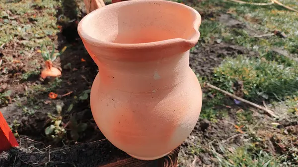 Antika kil sürahi. Ahşap bir çitin üzerindeki kil sürahi bahçedeki bir ağacın arka planına karşı. Kadim büyük kavanoz, içme suyu, su kaynağı, akan su, musluk suyu. Retro biçimi.