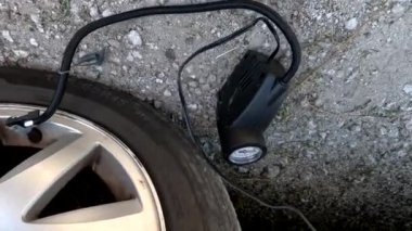 Bir adam kompresörle araba tekerleğini şişiriyor. Lastik şişirmek için küçük bir araba hava kompresörü. Şişirilmiş araba tekerlekleri. Araba tekerleğindeki hava basıncını kontrol ediyorum..