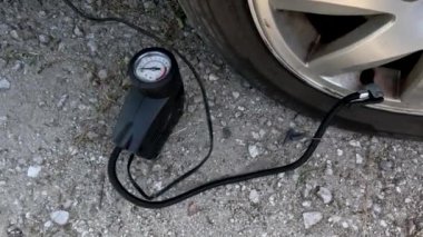 Bir adam kompresörle araba tekerleğini şişiriyor. Lastik şişirmek için küçük bir araba hava kompresörü. Şişirilmiş araba tekerlekleri. Araba tekerleğindeki hava basıncını kontrol ediyorum..