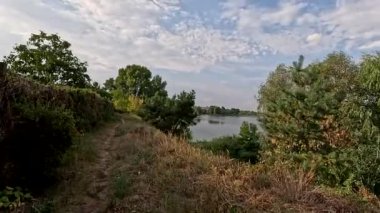 Sonbaharda yol boyunca yürüyorum. Sonbahar manzarası. Sonbahar yaprakları yerde. Dar yol. Nehir kenarında yürüyüş. Göl ve gökyüzü. Güzel doğal manzara. HDR video 4K 60 fps.
