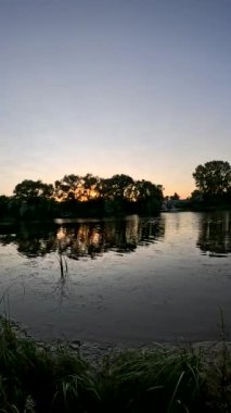 Nehirde gün batımı. Göl kıyısında gün doğumu. Güneş ağaçların arkasında. Gün batımı ve su ile güzel doğal manzara. Yüksek çözünürlüklü video Güneş suyun üzerinde parlıyor. Nehirdeki karanlık su.