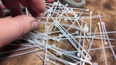 Beyaz kravatlar. Plastik kravatlar. Kahverengi ahşap arka planda beyaz naylon kablo bağları var. Yakın plan. Plastik kabloyu çelik yapının üzerine bağlıyorum.