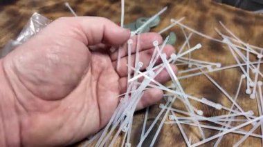 Beyaz kravatlar. Plastik kravatlar. Kahverengi ahşap arka planda beyaz naylon kablo bağları var. Yakın plan. Plastik kabloyu çelik yapının üzerine bağlıyorum.