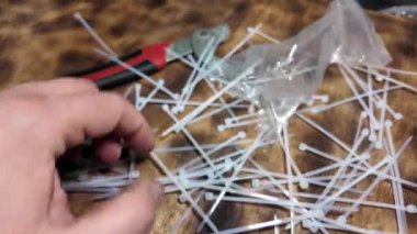 Beyaz kravatlar. Plastik kravatlar. Kahverengi ahşap arka planda beyaz naylon kablo bağları var. Yakın plan. Plastik kabloyu çelik yapının üzerine bağlıyorum.