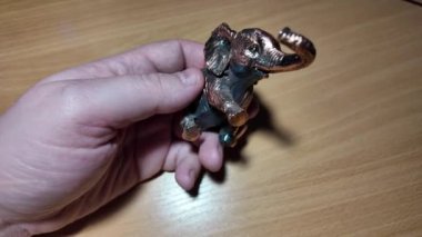 Fil heykelciği. Bakır metal fil heykeli. Oyuncak fil elinde. Bir insan titizlikle küçük fil heykelciklerini koyu ahşap bir rafa yerleştiriyor. Detaylı bir yakın çekim çekiyor.