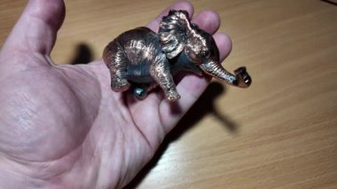 Fil heykelciği. Bakır metal fil heykeli. Oyuncak fil elinde. Bir insan titizlikle küçük fil heykelciklerini koyu ahşap bir rafa yerleştiriyor. Detaylı bir yakın çekim çekiyor.