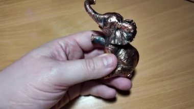 Fil heykelciği. Bakır metal fil heykeli. Oyuncak fil elinde. Bir insan titizlikle küçük fil heykelciklerini koyu ahşap bir rafa yerleştiriyor. Detaylı bir yakın çekim çekiyor.