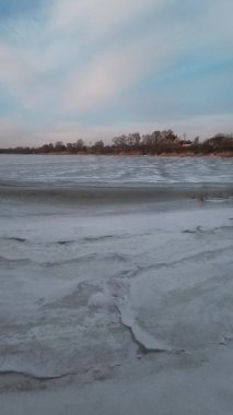 Nehirdeki buz. İlkbaharda buz yavaşça nehirde yüzüyor. Yüzen donmuş buz blokları olan nehir. Kıyıdaki karlar ve ağaçlar donuyor. Nehirdeki buz. dikey video 4k