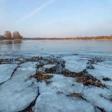 Nehirde buzla kaplı kış manzarası. Gölde çatlamış buz. Soğuk kış manzarası. Buz içinde donmuş ağaçlar. Su basmış ve donmuş toprak. Buzda kuşlar. Kış dönemi. Buzun bahar erimesi.