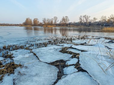 Nehirde buzla kaplı kış manzarası. Gölde çatlamış buz. Soğuk kış manzarası. Buz içinde donmuş ağaçlar. Su basmış ve donmuş toprak. Buzda kuşlar. Kış dönemi. Buzun bahar erimesi.