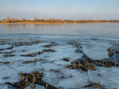 Nehirde buzla kaplı kış manzarası. Gölde çatlamış buz. Soğuk kış manzarası. Buz içinde donmuş ağaçlar. Su basmış ve donmuş toprak. Buzda kuşlar. Kış dönemi. Buzun bahar erimesi.