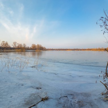 Nehirde buzla kaplı kış manzarası. Gölde çatlamış buz. Soğuk kış manzarası. Buz içinde donmuş ağaçlar. Su basmış ve donmuş toprak. Buzda kuşlar. Kış dönemi. Buzun bahar erimesi.