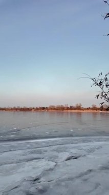 Nehirde buzla kaplı kış manzarası. Gölde çatlamış buz. Soğuk kış manzarası. Buz içinde donmuş ağaçlar. Su basmış ve donmuş toprak. Buzda kuşlar. Kış dönemi. Buzun bahar erimesi.