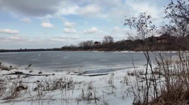 Donmuş göl üzerindeki ağır çekim kış manzarası. Nehirde buzlar kırıldı. Vahşi doğada kuş gözlemciliği. 4K 'de ağır çekim videosu. Göl kıyısının soğuk kış soğuğunun elde tutulan videosu.