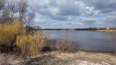 Bahar doğası. Bahar doğasında yürüyüş. İlkbaharda nehir boyunca bir patika. Nehir kenarında yürüyüş. Güzel gökyüzü ve göl. Yavaş çekim videosu.