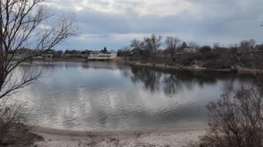 Göl kıyısındaki manzara. Nehirdeki yansıma. Nehrin kumlu kıyısı ve karanlık su. Doğa manzarası. Denize doğru yürü. Suda küçük dalgalar.