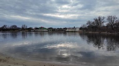 Göl kıyısındaki manzara. Nehirdeki yansıma. Nehrin kumlu kıyısı ve karanlık su. Doğa manzarası. Denize doğru yürü. Suda küçük dalgalar.