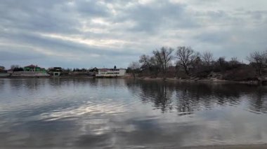 Göl kıyısındaki manzara. Nehirdeki yansıma. Nehrin kumlu kıyısı ve karanlık su. Doğa manzarası. Denize doğru yürü. Suda küçük dalgalar.