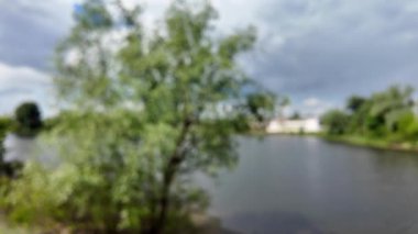 Bulanık arkaplan, gökyüzü ve nehir. Soyut doğa geçmişi. Nehir kıyısında bulanık bir video. Gökyüzüne karşı uzun ağaçlar. Ormanda yavaş çekim videosu. Kum ve nehir. Suyun üzerindeki bulutlu gökyüzü.