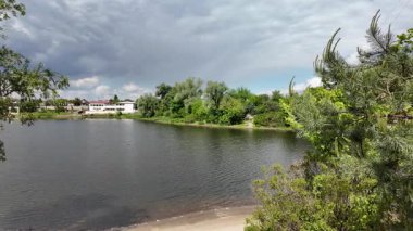 Nehir ve kasvetli gökyüzü manzarası. Yavaş çekim video doğa manzarası. Yağmurdan önce hava durumu. Fırtınadan önce gökyüzü. Güneş ve yoğun yağmur bulutları. Nehir ve kumlu sahil. Nehirde karanlık su.