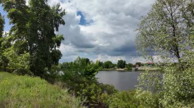 Nehir ve kasvetli gökyüzü manzarası. Yavaş çekim video doğa manzarası. Yağmurdan önce hava durumu. Fırtınadan önce gökyüzü. Güneş ve yoğun yağmur bulutları. Nehir ve kumlu sahil. Nehirde karanlık su.