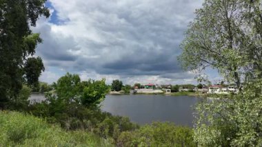 Nehir ve kasvetli gökyüzü manzarası. Yavaş çekim video doğa manzarası. Yağmurdan önce hava durumu. Fırtınadan önce gökyüzü. Güneş ve yoğun yağmur bulutları. Nehir ve kumlu sahil. Nehirde karanlık su.