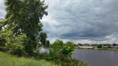 Nehir ve kasvetli gökyüzü manzarası. Yavaş çekim video doğa manzarası. Yağmurdan önce hava durumu. Fırtınadan önce gökyüzü. Güneş ve yoğun yağmur bulutları. Nehir ve kumlu sahil. Nehirde karanlık su.