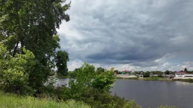 Nehir ve kasvetli gökyüzü manzarası. Yavaş çekim video doğa manzarası. Yağmurdan önce hava durumu. Fırtınadan önce gökyüzü. Güneş ve yoğun yağmur bulutları. Nehir ve kumlu sahil. Nehirde karanlık su.