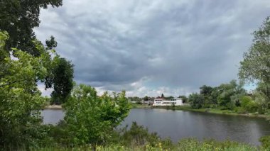 Nehir ve kasvetli gökyüzü manzarası. Yavaş çekim video doğa manzarası. Yağmurdan önce hava durumu. Fırtınadan önce gökyüzü. Güneş ve yoğun yağmur bulutları. Nehir ve kumlu sahil. Nehirde karanlık su.