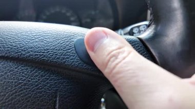 Şoför kornaya basar. Şoför araba sürerken korna çalar. Şoför direksiyonu tutuyor..