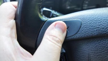 Şoför kornaya basar. Şoför araba sürerken korna çalar. Şoför direksiyonu tutuyor..
