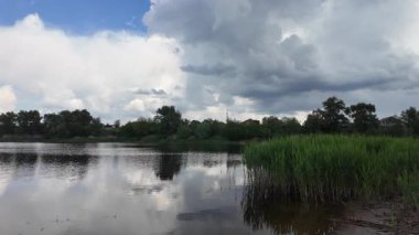 Bulutlar suda yansıyor. Gökyüzü ve nehir. Göllü doğal manzara. Göl üzerinde yağmur bulutları. Nehirdeki pürüzsüz karanlık su. Yavaş çekim video doğal manzara. doğa arkaplanı.