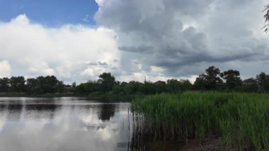 Bulutlar suda yansıyor. Gökyüzü ve nehir. Göllü doğal manzara. Göl üzerinde yağmur bulutları. Nehirdeki pürüzsüz karanlık su. Yavaş çekim video doğal manzara. doğa arkaplanı.