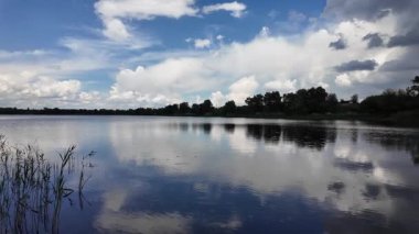 Bulutlar suda yansıyor. Gökyüzü ve nehir. Göllü doğal manzara. Göl üzerinde yağmur bulutları. Nehirdeki pürüzsüz karanlık su. Yavaş çekim video doğal manzara. doğa arkaplanı.