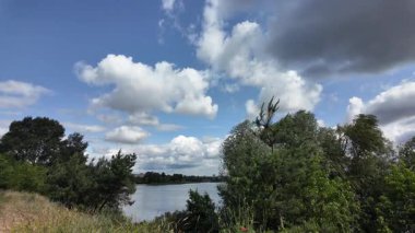 Nehrin kıyısına yürü. Göl kıyısı. Nehir kıyısında. Çimenler ve ağaçlar gölün kıyısında yetişir. Söğütlerin dalları suyun üzerinde uzanıyor. Uzak sahilde apartmanlar var..