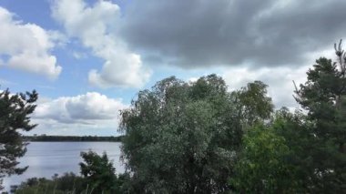 Nehrin kıyısına yürü. Göl kıyısı. Nehir kıyısında. Çimenler ve ağaçlar gölün kıyısında yetişir. Söğütlerin dalları suyun üzerinde uzanıyor. Uzak sahilde apartmanlar var..