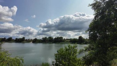 Nehrin kıyısına yürü. Göl kıyısı. Nehir kıyısında. Çimenler ve ağaçlar gölün kıyısında yetişir. Söğütlerin dalları suyun üzerinde uzanıyor. Uzak sahilde apartmanlar var..