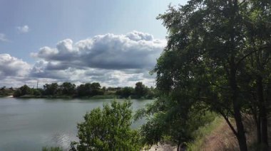 Nehrin kıyısına yürü. Göl kıyısı. Nehir kıyısında. Çimenler ve ağaçlar gölün kıyısında yetişir. Söğütlerin dalları suyun üzerinde uzanıyor. Uzak sahilde apartmanlar var..