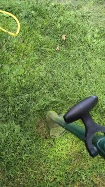 Bahçıvan uzun yeşil çimenleri biçer, erkeksi elleri tutar, çim biçme makinesi, farklı yönlerde uçan yabani otlar, yakın plan