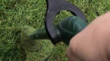 Bahçıvan uzun yeşil çimenleri biçer, erkeksi elleri tutar, çim biçme makinesi, farklı yönlerde uçan yabani otlar, yakın plan