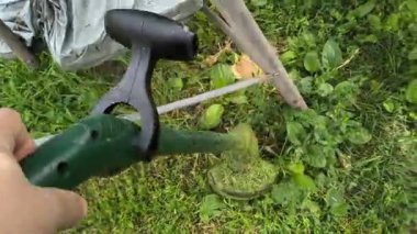 Bahçıvan uzun yeşil çimenleri biçer, erkeksi elleri tutar, çim biçme makinesi, farklı yönlerde uçan yabani otlar, yakın plan