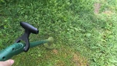 Bahçıvan uzun yeşil çimenleri biçer, erkeksi elleri tutar, çim biçme makinesi, farklı yönlerde uçan yabani otlar, yakın plan