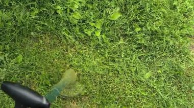 Bahçıvan uzun yeşil çimenleri biçer, erkeksi elleri tutar, çim biçme makinesi, farklı yönlerde uçan yabani otlar, yakın plan