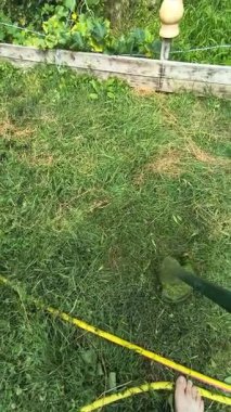 Bahçıvan uzun yeşil çimenleri biçer, erkeksi elleri tutar, çim biçme makinesi, farklı yönlerde uçan yabani otlar, yakın plan