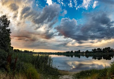 Çok güzel bir gün batımı ve su. Yaz akşamı manzarası. Sudaki bulutların yansıması. Güneş ufukta batıyor. Göllü yaz manzarası. Sudaki ağaçların yansıması. Nehirde gün doğumu. şehvetli bulutlar.