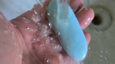 Elinde mavi sabun var. Adam ellerini mavi sabunla yıkıyor. Lavaboya su damlıyor. İnsan eliyle akan su..