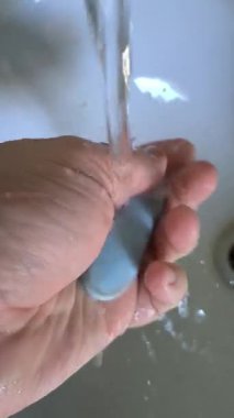 Elinde mavi sabun var. Adam ellerini mavi sabunla yıkıyor. Lavaboya su damlıyor. İnsan eliyle akan su..